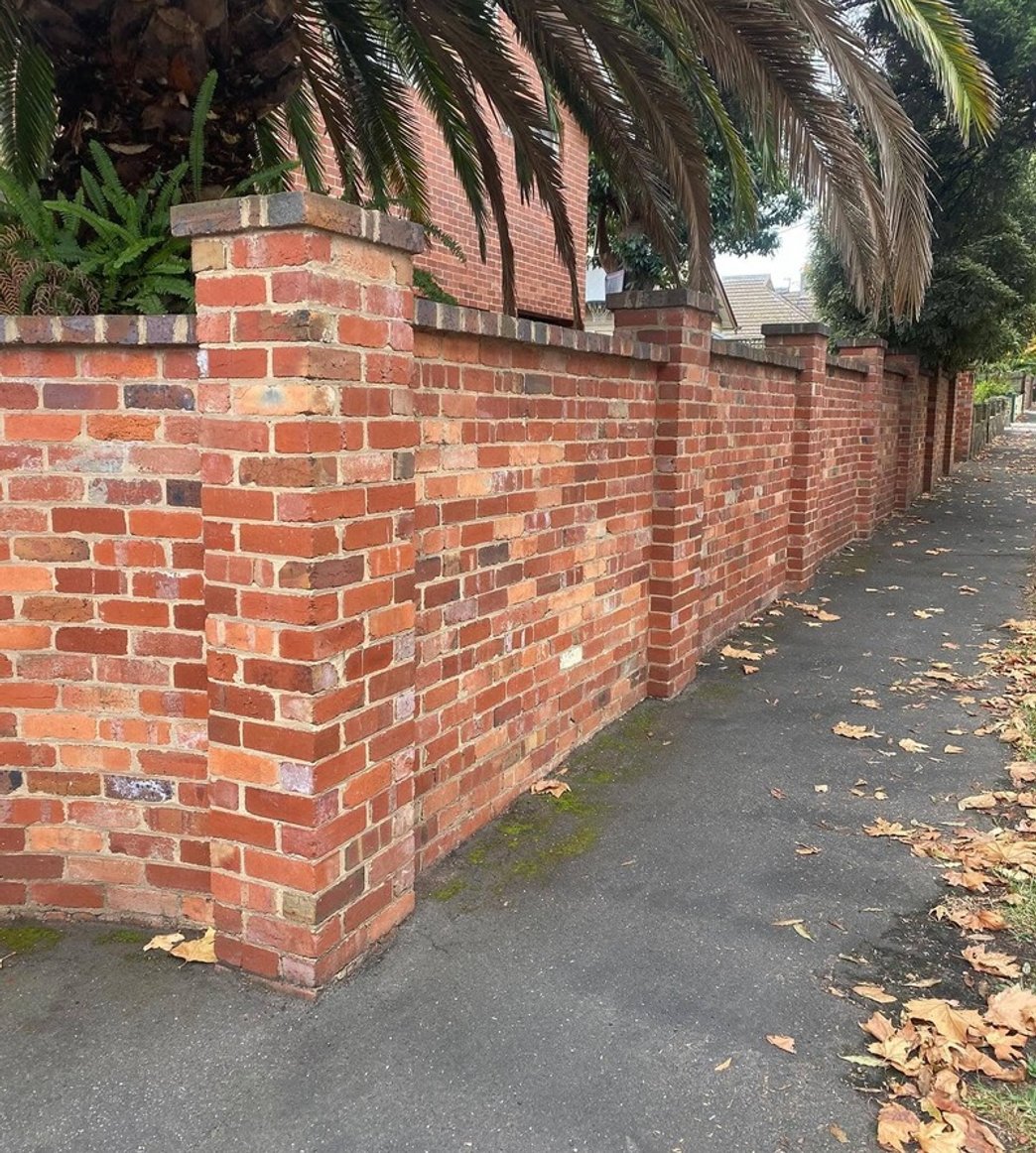 Decorative red brick boundary fence with pillars and capping along a sidewalk