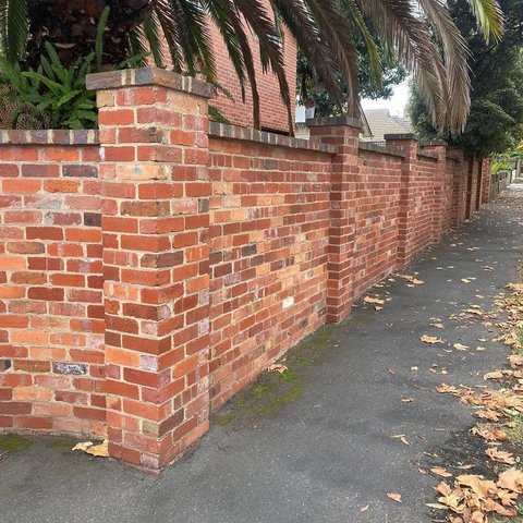 Decorative red brick boundary fence with pillars and capping along a sidewalk