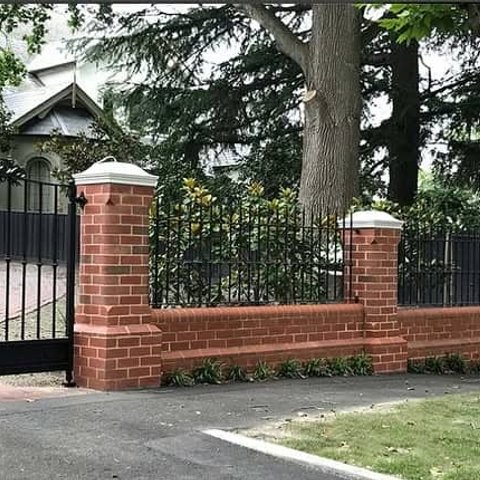 Ornate red brick fence with white capped pillars and wrought iron gate