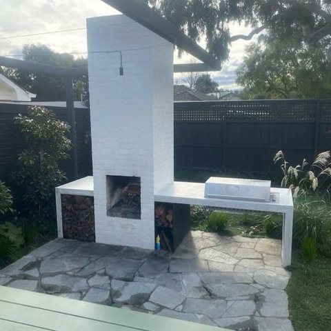 White painted outdoor brick fireplace with built in barbecue and wood storage