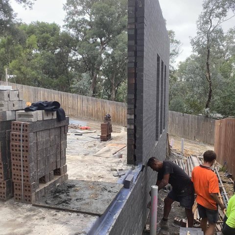 Tall charcoal brick feature wall with narrow window openings under construction