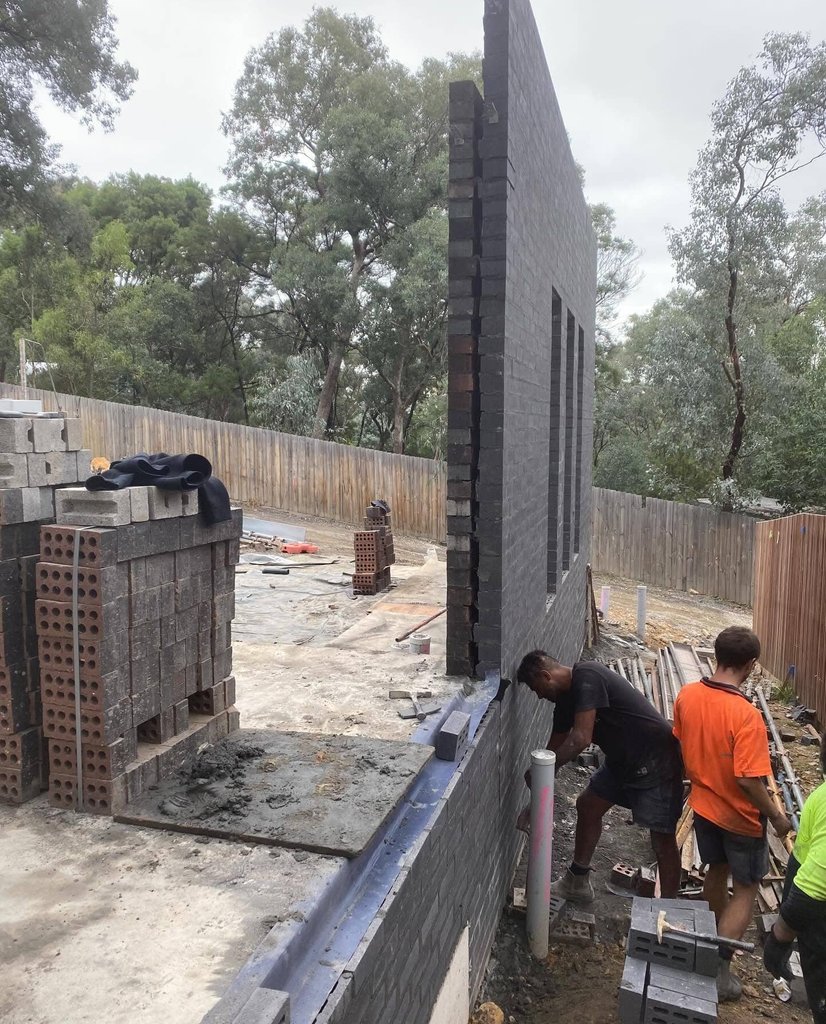 Tall charcoal brick feature wall with narrow window openings under construction