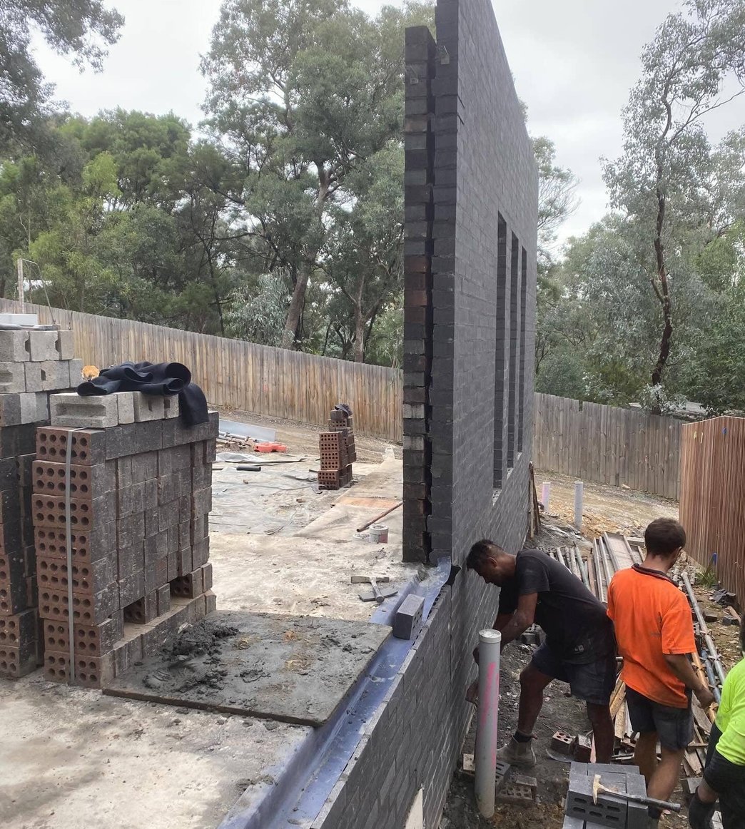 Tall charcoal brick feature wall with narrow window openings under construction