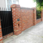 Red brick fence with black iron gate by Alternative Bricklaying Red brick fence with black iron gate